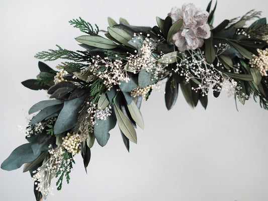 Weihnachtsdekoration Tischdekoration: Stehender Trockenblumenkranz gebunden an einen Metallring aus haltbaren Olivenzweigen, Eukalyptus und Tanne Thuja. Christbaumkugeln und Häuschen