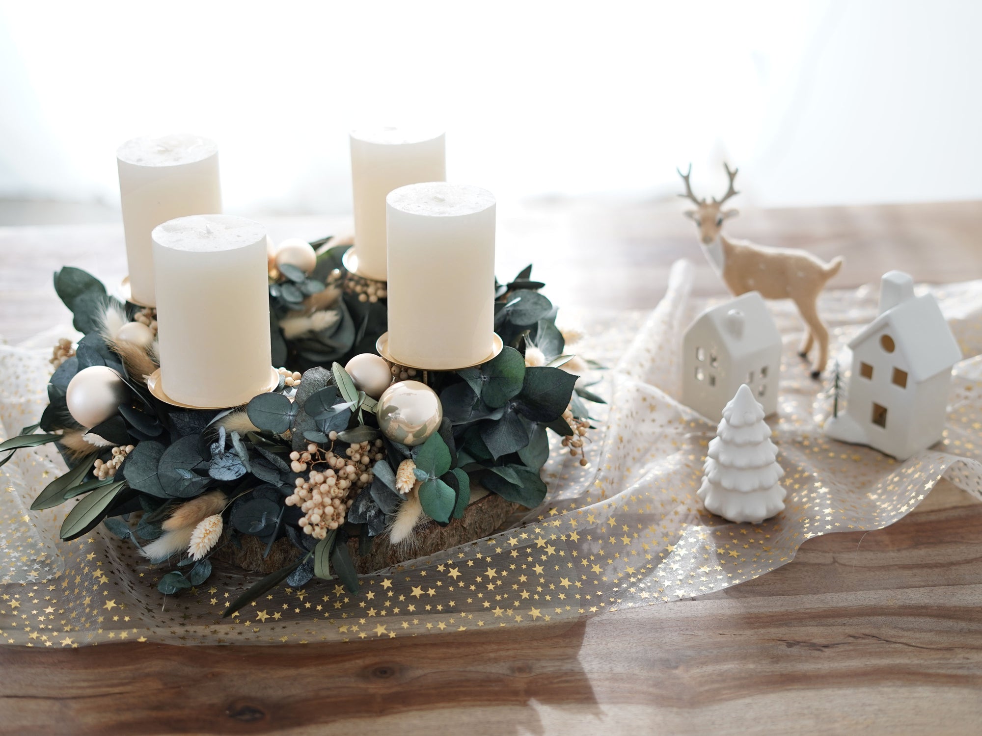 Stilvoll dekorierter Adventskranz aus Trockenblumen, Eukalyptus und Olivenzweigen mit Stumpenkerzen und Weihnachtskugeln in festlicher Wohnatmosphäre