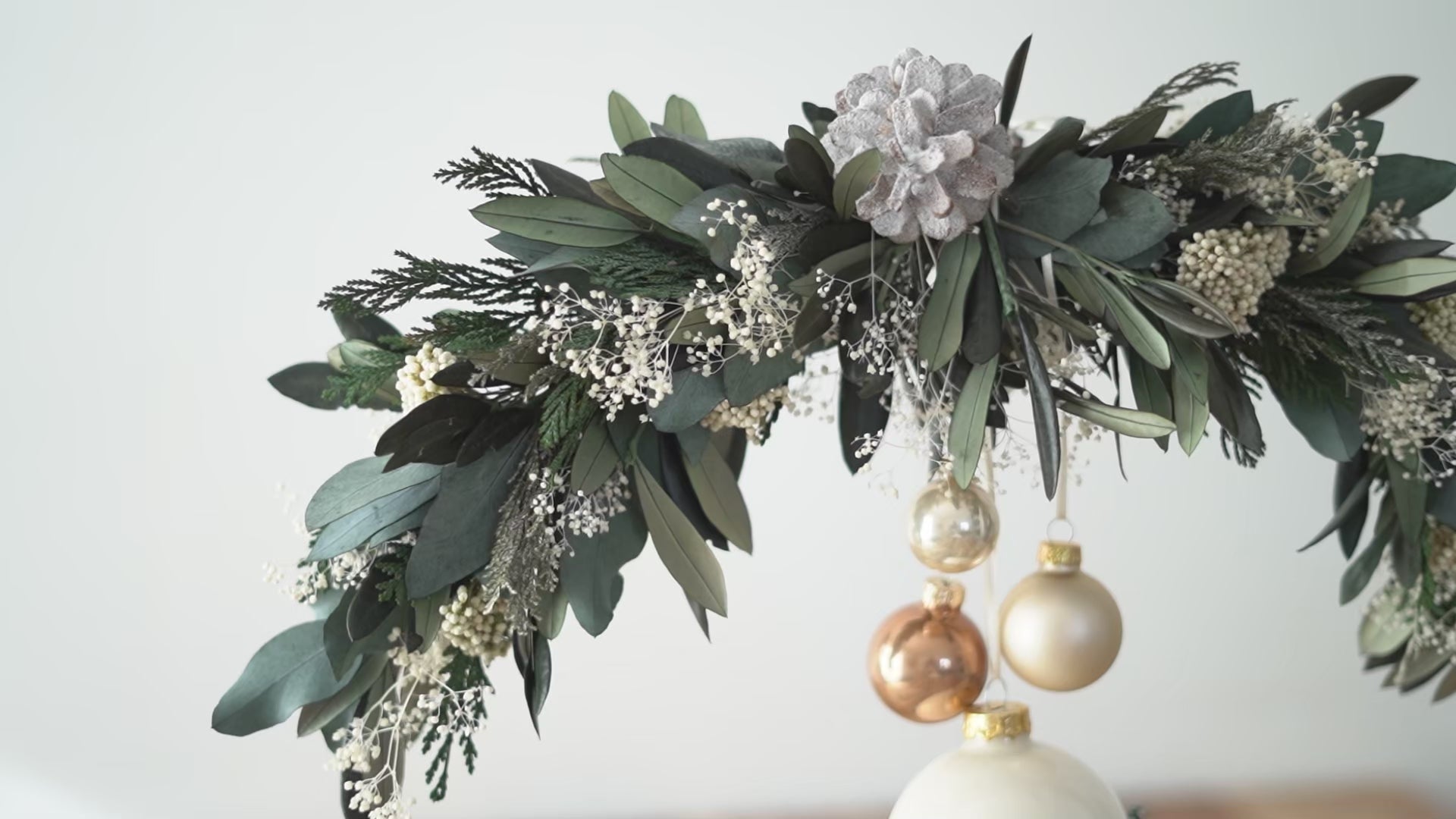 Video laden: Weihnachtsdekoration Tischdekoration: Stehender Trockenblumenkranz gebunden an einen Metallring aus haltbaren Olivenzweigen, Eukalyptus und Tanne Thuja. Christbaumkugeln und Häuschen